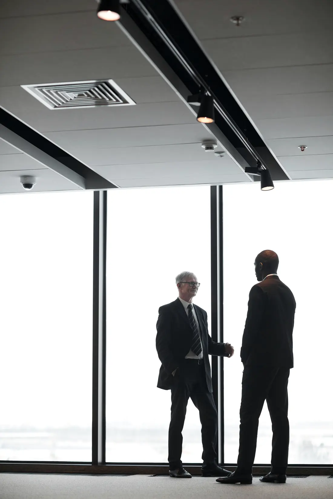 Dois executivos conversam diante da janela de um andar corporativo vazio